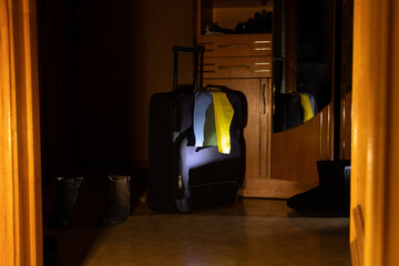 A suitcase stands at the door of an apartment with the flag of Ukraine and a passport in the dark...