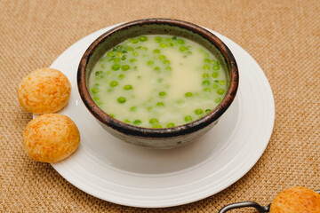 Celery cream soup with a green pea in a bowl garnished with chopped green onion and served with freshly baked cheese bread close-up
