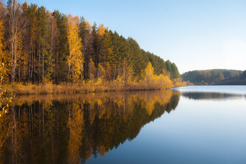 Colorful foliage tree reflections in calm pond water on a beautiful autumn day. A quiet and beautiful place to relax.