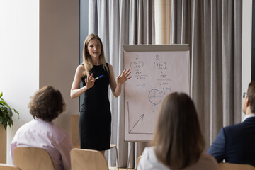 Professional seminar, corporate training event for company staff in board room. Confident female team leader or coach express opinion, share strategy on flip chart during teambuilding with employees