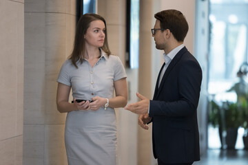Two businesspeople, female male partners, serious colleagues talking meet in modern office hallway. Teammates discussing common project, share information, thoughts during break in company workspace