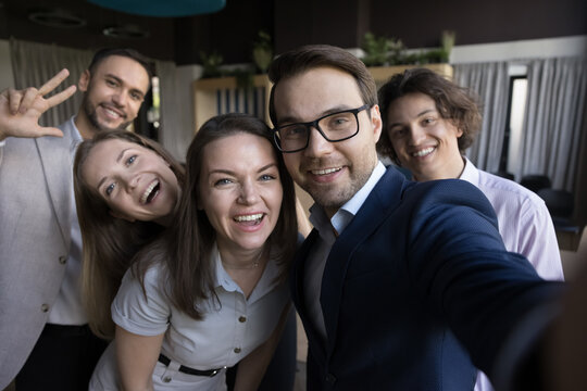 Five happy business people in formal wear making selfie picture, holding device, smiling faces looking at smartphone screen pose together in office, use modern tech, having fun, showing companionship