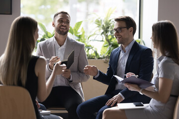 Four millennial professional teammates solve business gathered in briefing, informal meeting smile...