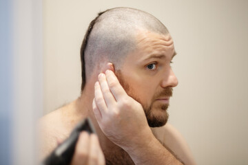 home haircut, a man cuts his head with a clipper in front of a mirror