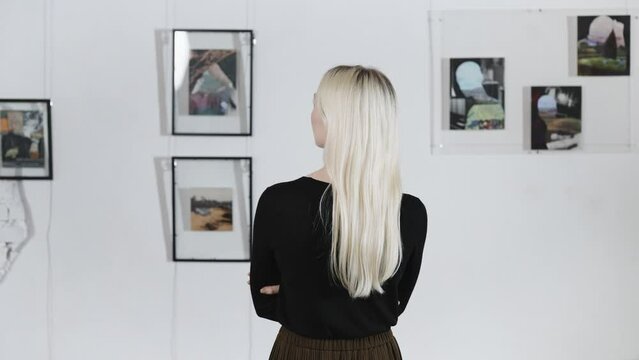 Blonde back, in the art gallery. A woman poses against the backdrop of abstract paintings by a contemporary artist.