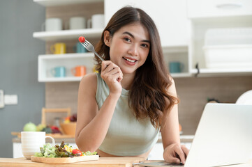 Portrait Happy Asia woman look at camera with salad and computer notebook in kitchen room