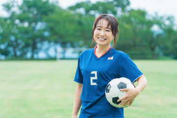 サッカーボールを持ちながら笑顔でサッカーするファン・サポーターの日本人女性  © buritora