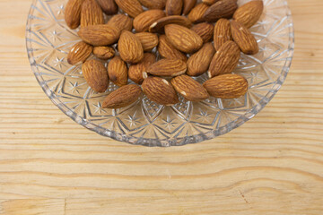 Roasted almonds in glass plate on wooden background