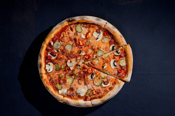 Appetizing pizza with hunting sausages, mozzarella cheese, pickled cucumbers, chili peppers on a...