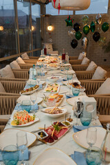 Festive table with appetizers. Salads, caviar, cheese and meat plates. Empty glasses, plates, chairs with cushions for guests. Balloons on background