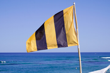 Warning flag yellow black vertical line waving on coast beach on sunny day