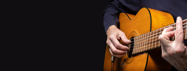 Guitarist playing acoustic guitar on black background, selective focus. A male musician plays the guitar. cover for online courses learning at home. A man playing guitar. Long wide banner, copy space