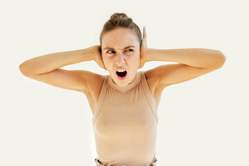 Young annoyed frustrated female can't stand loud disgusting noise or sounds, covering her ears, shouting with rage and fury, looking aside, suffering from headache or migraine, isolated on white