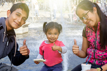 mexican family in park looking at the camera and making the sign of like with their hands