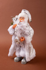 A funny Santa Claus toy with a bag of gifts on its back and a Christmas tree in its hand and white pants.