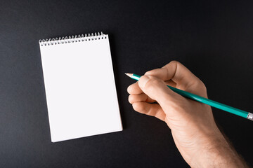 Hand with a pencil writes in a blank notebook