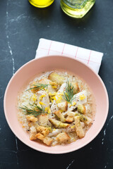 Chicken soup with croutons and white rice served in a roseate bowl, vertical shot on a black marble background, elevated view