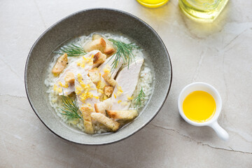 Bowl of soup with chicken breast, rice and croutons, horizontal shot on a beige stone background, elevated view