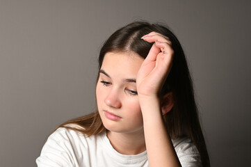 Fototapeta premium Portrait of sad teen girl on gray background. Teenage girl looking thoughtful about troubles