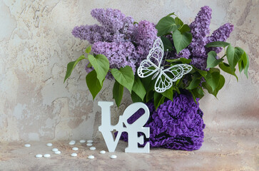 A bouquet of lilacs, decorative letters and a white butterfly on an abstract background. Holiday and love concept.