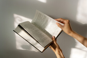 Fototapeta premium the girl flips through the pages of the book, on which the shadow from the window falls