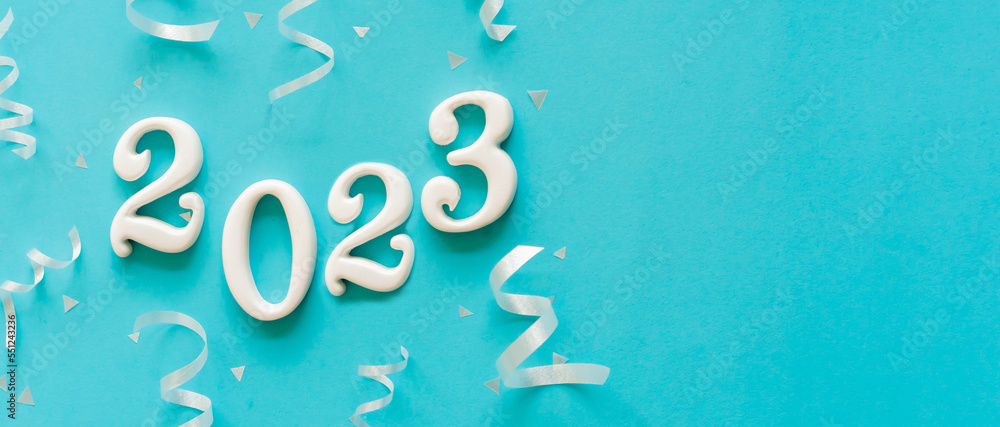 Wall mural close up number 2023 shape wood on blue color background with rolling ribbon and confetti for happy 