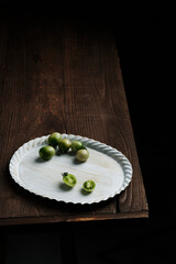 Fototapeta na wymiar Small green tomatoes in artistic white tray on wooden table edge