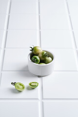 a colorful saucer fill with green tomatoes on white tiles background