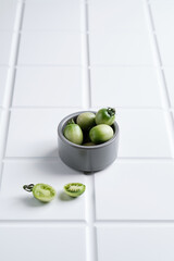 a colorful saucer fill with green tomatoes on white tiles background