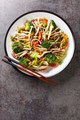 Stir Fried vegetables carrots, peppers, cabbage, broccoli and shimeji beech mushrooms close-up in a plate on the table. Vertical top view from above