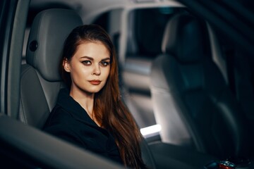 a stylish, luxurious woman is sitting in a black car at night in the passenger seat, looking at the camera in a relaxed way. Topics of safe driving on the roads