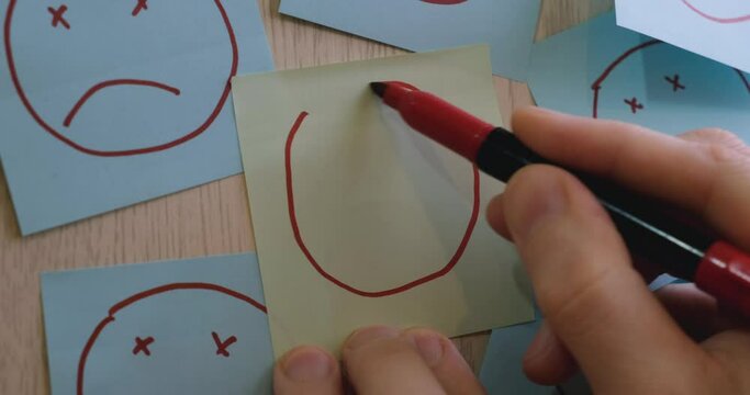 Man drawing funny smiling face with red marker on yellow sticky note on wall. Motivation, success, psychology and emotion concepts