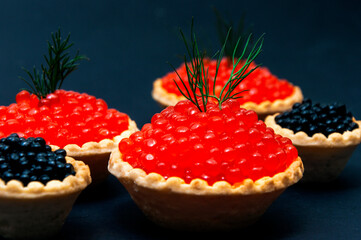 Red and black caviar in tartlets on a black background.