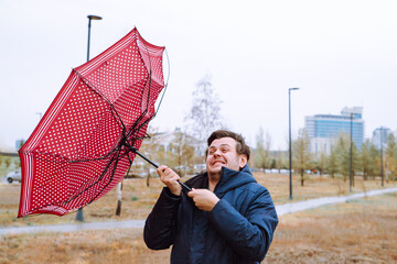 Shocked young caucasian european white male man with broken umbrella in city park, strong storm...