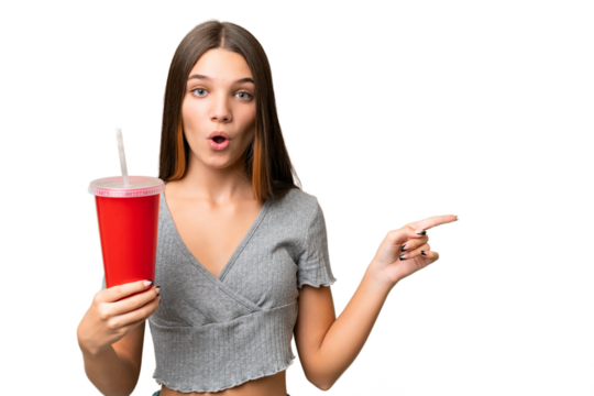 Teenager caucasian girl holding a soda over isolated background surprised and pointing side