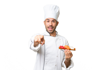 Young caucasian chef holding a sushi over isolated background surprised and pointing front