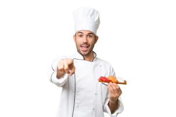 Papier Peint photo Bar à sushi Young caucasian chef holding a sushi over isolated background surprised and pointing front