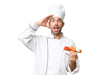 Young caucasian chef holding a sushi over isolated background with surprise expression