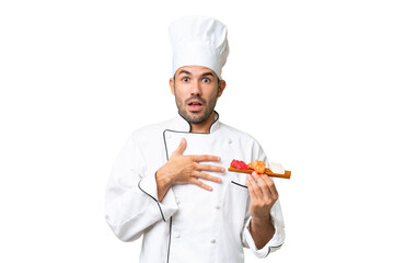 Young caucasian chef holding a sushi over isolated background surprised and shocked while looking right