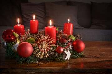 Advent wreath with four burning red candles and Christmas decoration on a wooden table in front of...