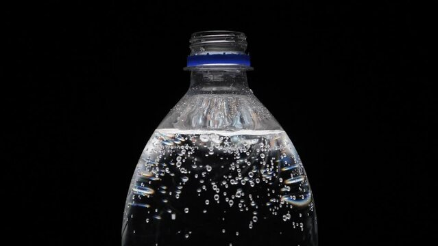 A bottle of carbonated water is unscrewed by hand on a black background. Bubbles come out of the bottle. Pure mineralized water with gas. Man opens plastic bottle of carbonated water, black background