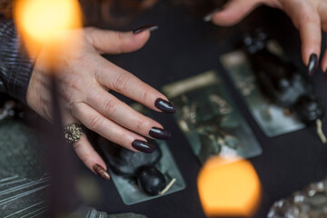 Fototapeta na wymiar Fortune teller's hands with black manicure over tarot cards in candle count. Magic, rituals and the occult. Close-up.