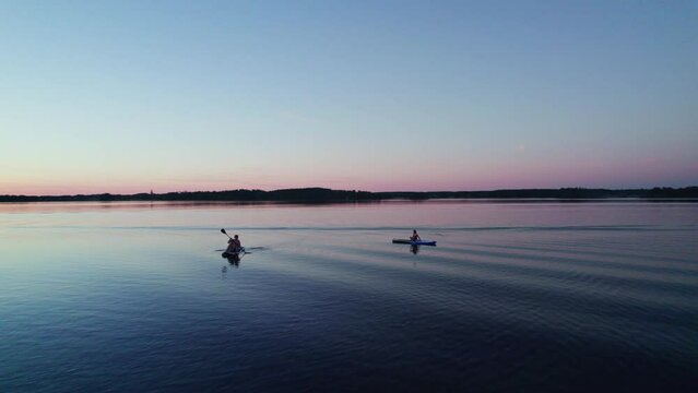 Woman with children sit and paddle on inflatable sup boards on a lake. Low angle view. orbit shot. Active summer vacation during midsummer blue hour. Näs bruk, Dalarna Sweden