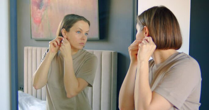 Woman putting on the jewellery while standing in front the mirror in her bed room preparing to go out
