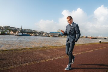 Young businessman walking casually while looking at his phone. Businessman closely following his business