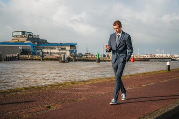 Young businessman walking casually while looking at his phone. Businessman closely following his business