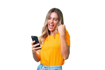 Young Uruguayan woman over isolated background with phone in victory position