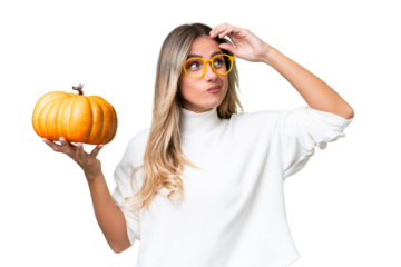 Young Uruguayan woman holding a pumpkin over isolated background having doubts and with confuse face expression