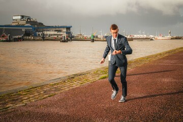 Young businessman running on the docks in town. Late businessman looking at his watch while running