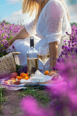 Wicker basket with delicious food for a romantic picnic in a lavender field. The girl pours wine.